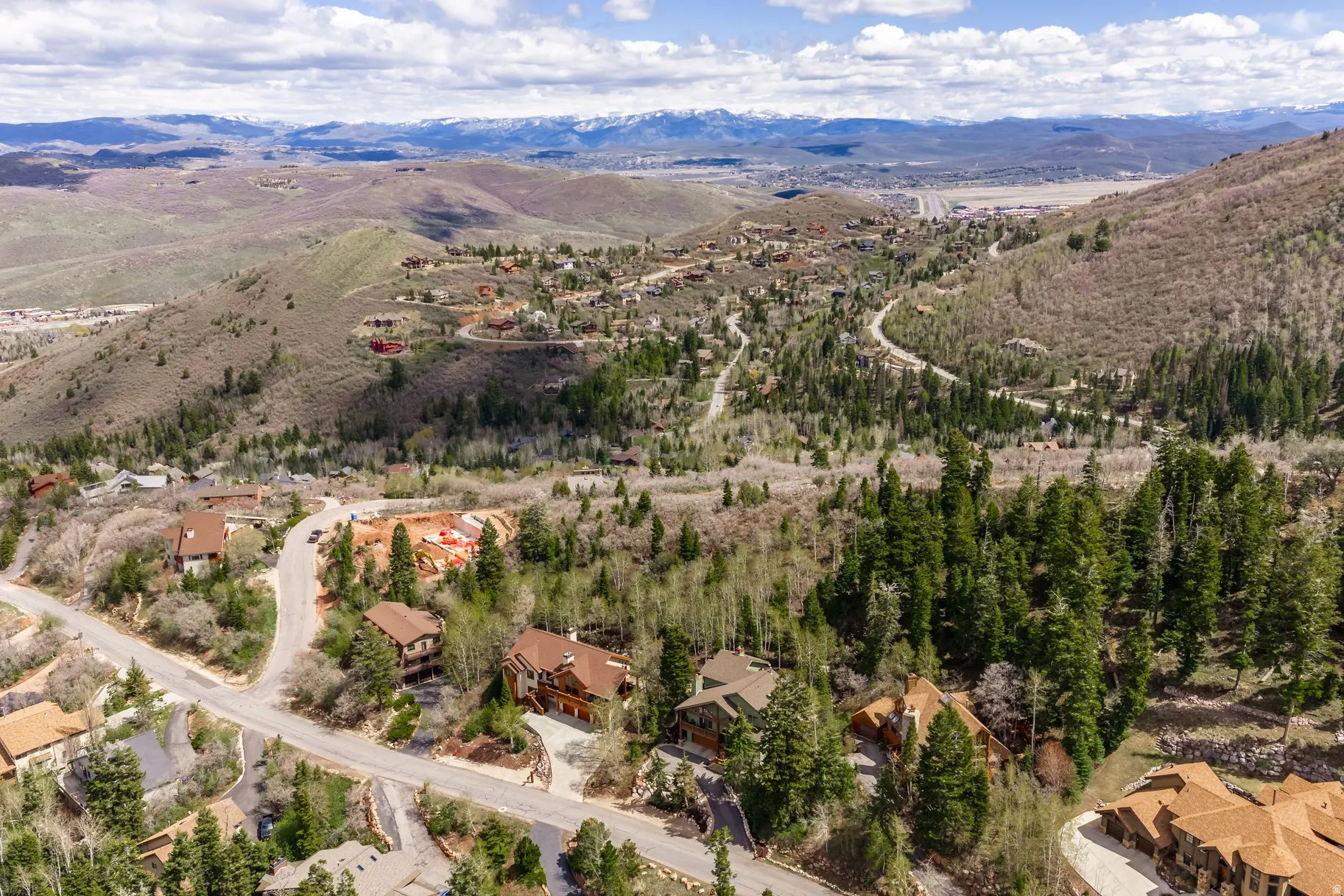 Elevated mountain community featuring established homes, winding roads, abundant mature trees, surrounding natural landscapes, and distant snow-capped peaks