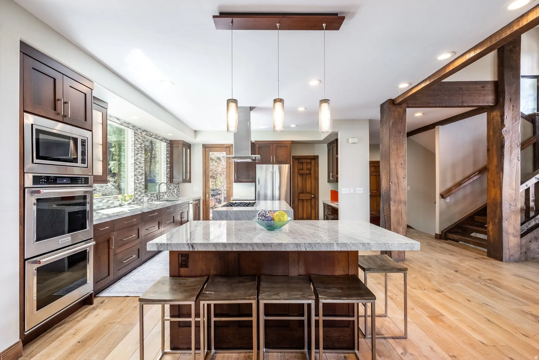 Gourmet kitchen featuring a large stone-top island, stainless steel double ovens, built-in microwave, and wood-finish cabinetry