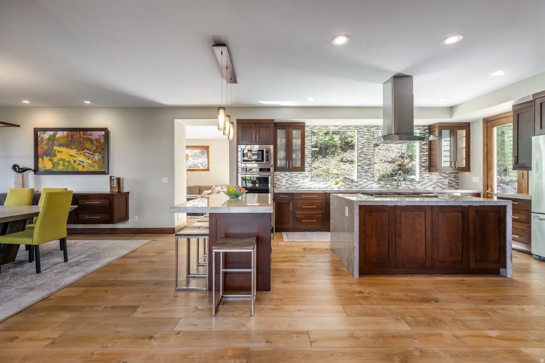 Contemporary kitchen featuring wood-finish flooring, dark wood cabinetry, a stainless steel range hood, and a light-toned tile backsplash