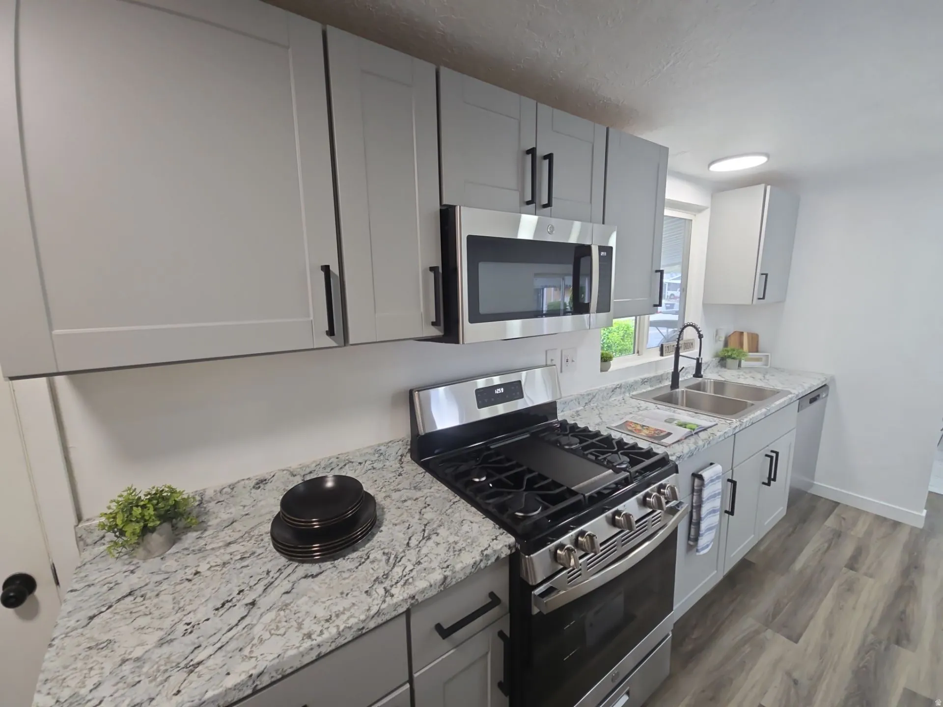 Kitchen featuring stainless steel appliances, gray cabinets, dark wood finished floors, and light stone counters