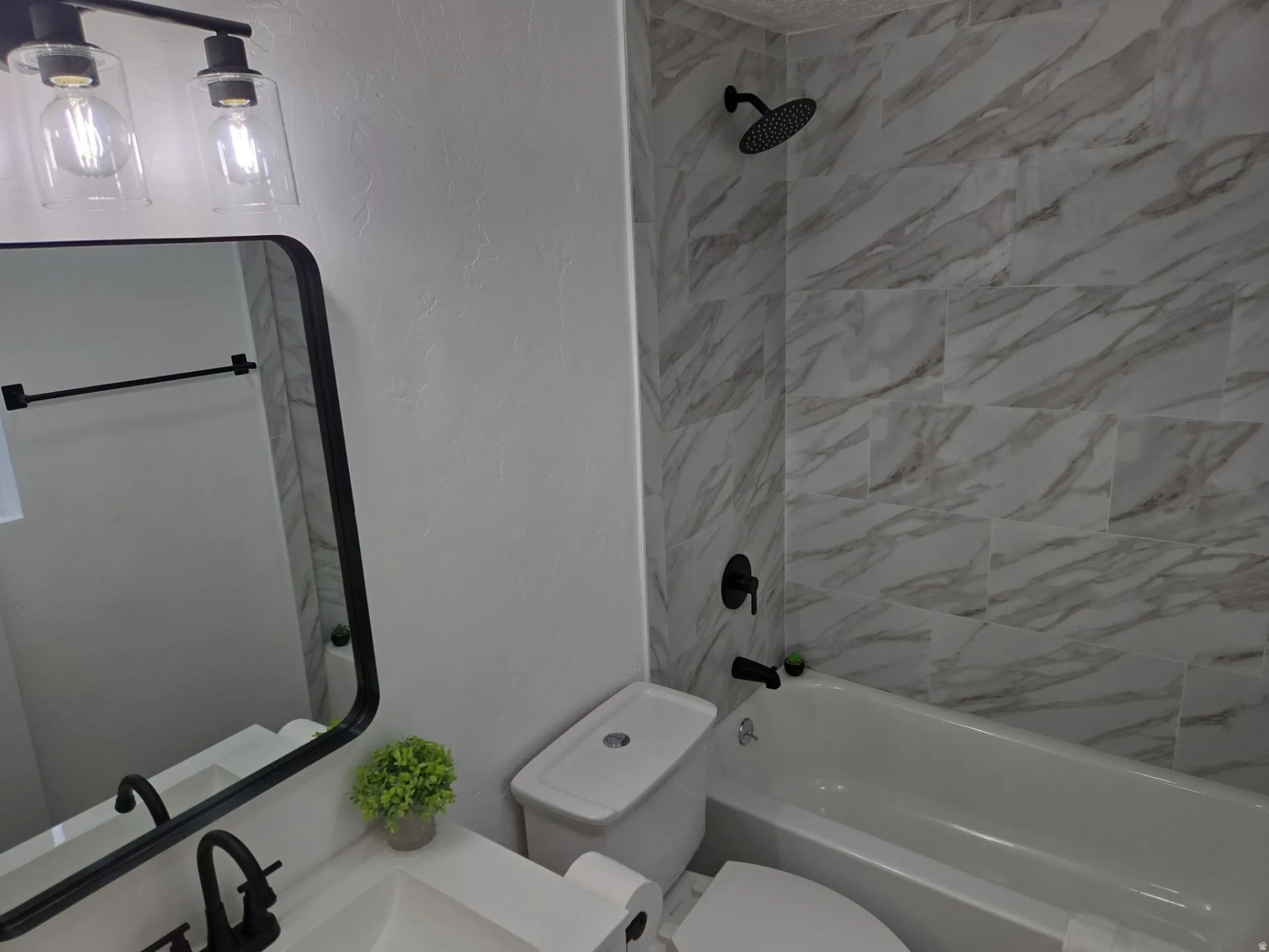Bathroom with a textured wall, vanity, and shower / washtub combination
