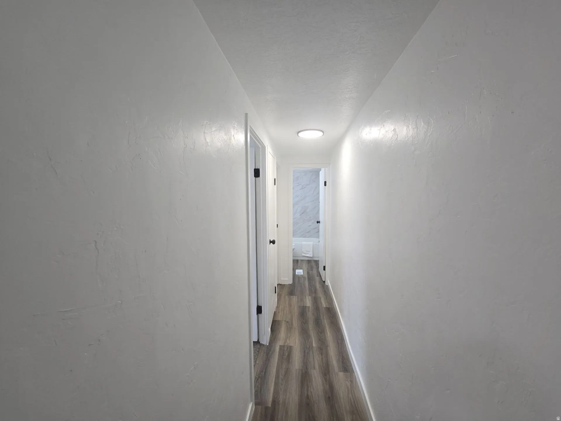Corridor with a textured wall, dark wood-style floors, and a textured ceiling