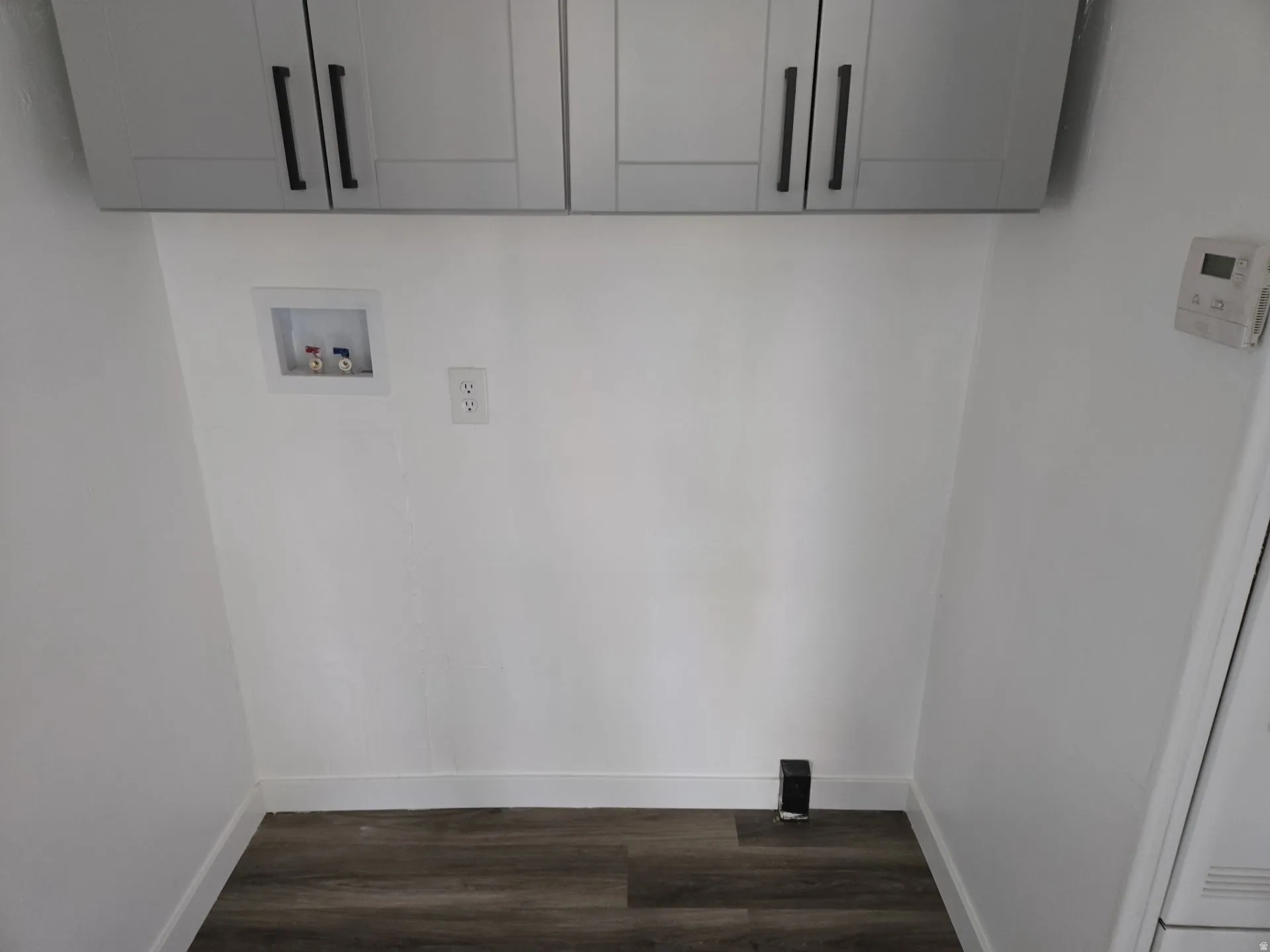 Laundry area featuring dark wood finished floors, cabinet space, and washer hookup