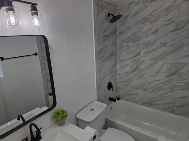 Bathroom with a textured wall, vanity, and shower / washtub combination