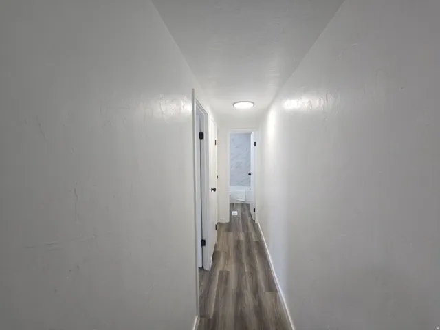 Corridor with a textured wall, dark wood-style floors, and a textured ceiling