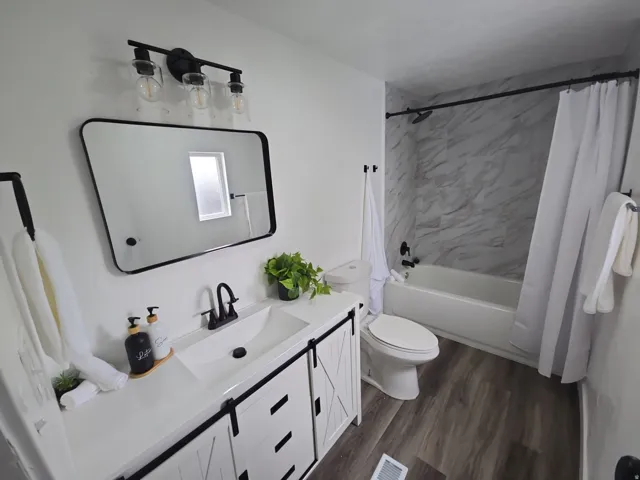 Bathroom with vanity, shower / bath combination with curtain, and dark wood-style floors