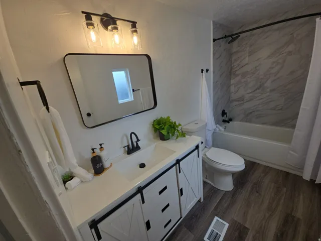 Full bathroom with vanity, dark wood-type flooring, and shower / bathtub combination with curtain