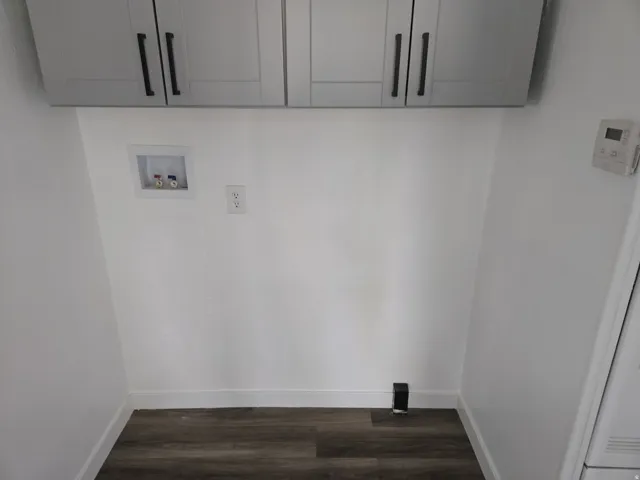 Laundry area featuring dark wood finished floors, cabinet space, and washer hookup
