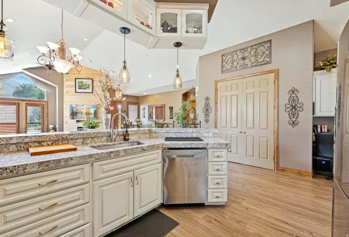 Kitchen with cream cabinets, dishwasher, light wood-type flooring, glass insert cabinets, and vaulted ceiling
