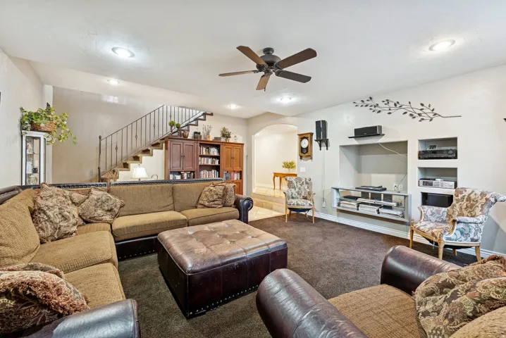 Living area with arched walkways, ceiling fan, carpet, and built in features