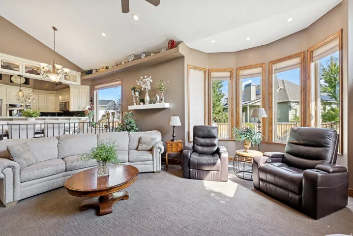 Living area with suspended lighting, carpet floors, ceiling fan, and lofted ceiling