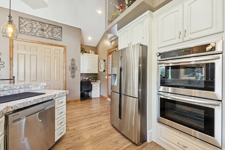 Kitchen featuring stainless steel appliances, white cabinetry, light wood finished floors, pendant lighting, and built in desk