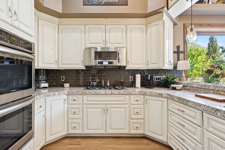 Kitchen featuring stainless steel appliances, decorative light fixtures, white cabinetry, tasteful backsplash, and light wood-style floors