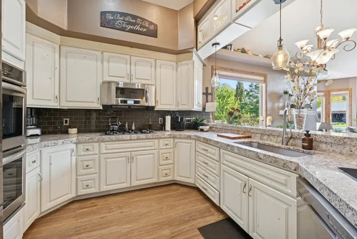 Kitchen featuring light wood-style floors, stainless steel appliances, suspended lighting, and decorative backsplash