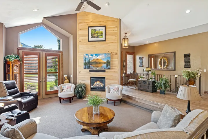 Carpeted living room with a large fireplace, lofted ceiling, recessed lighting, ceiling fan, and wood walls