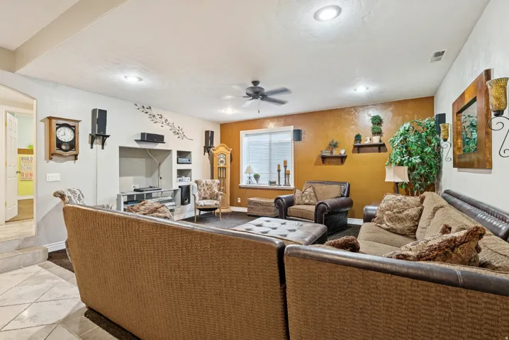 Tiled living area with a ceiling fan and baseboards