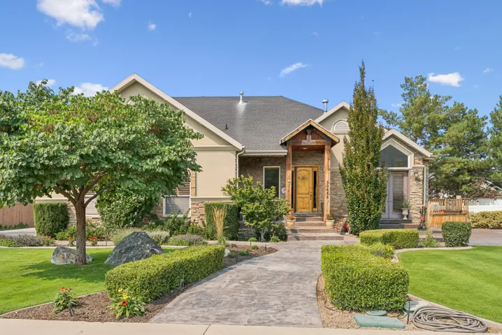 View of front facade featuring a front yard, stone siding, roof with shingles, and stucco siding