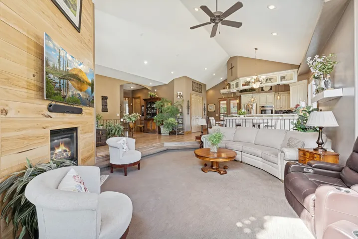 Living room featuring a fireplace, hanging lights, ceiling fan, carpet flooring, and lofted ceiling