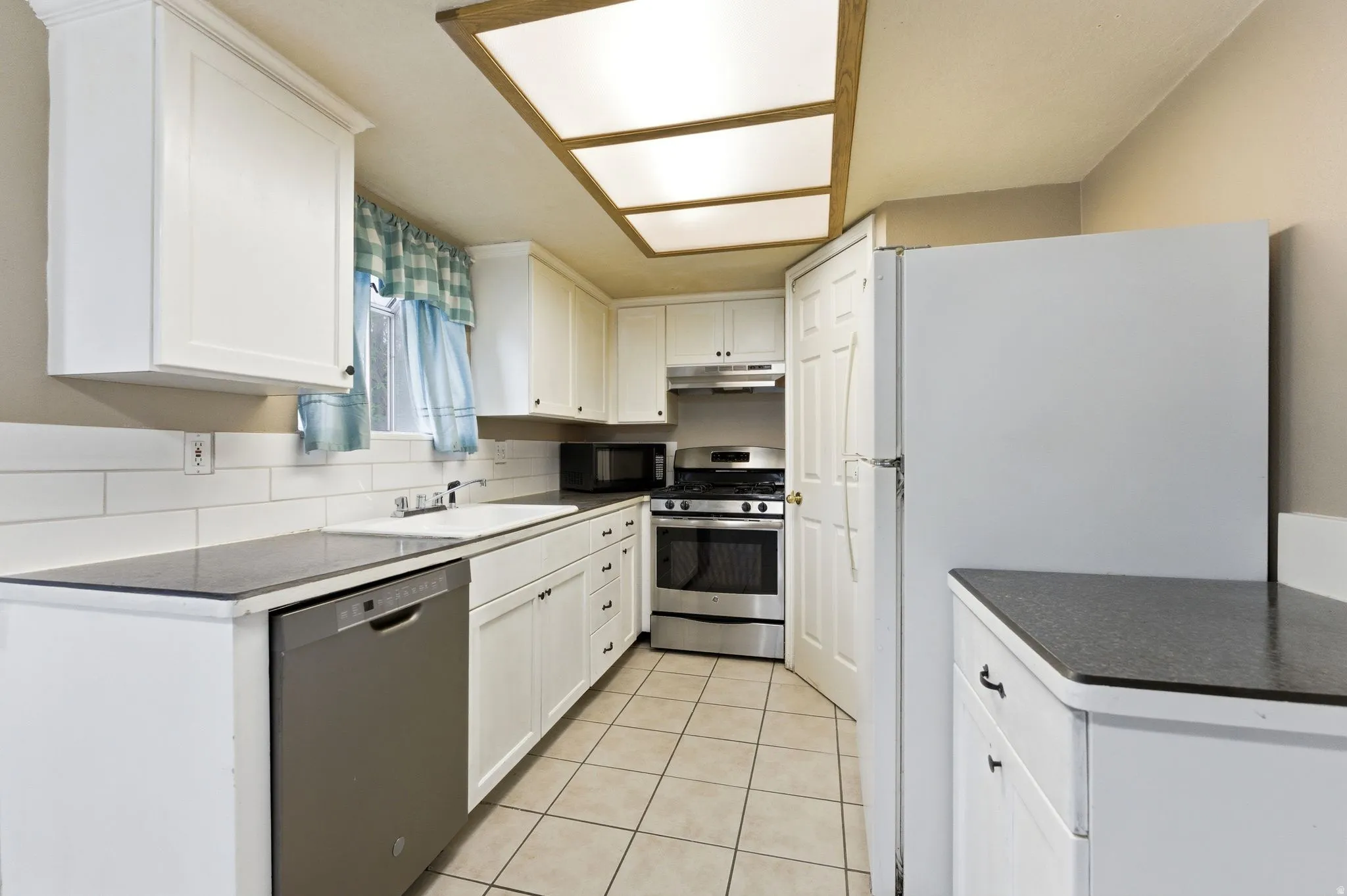 Kitchen featuring stainless steel appliances, white cabinetry, dark countertops, and light tile patterned flooring