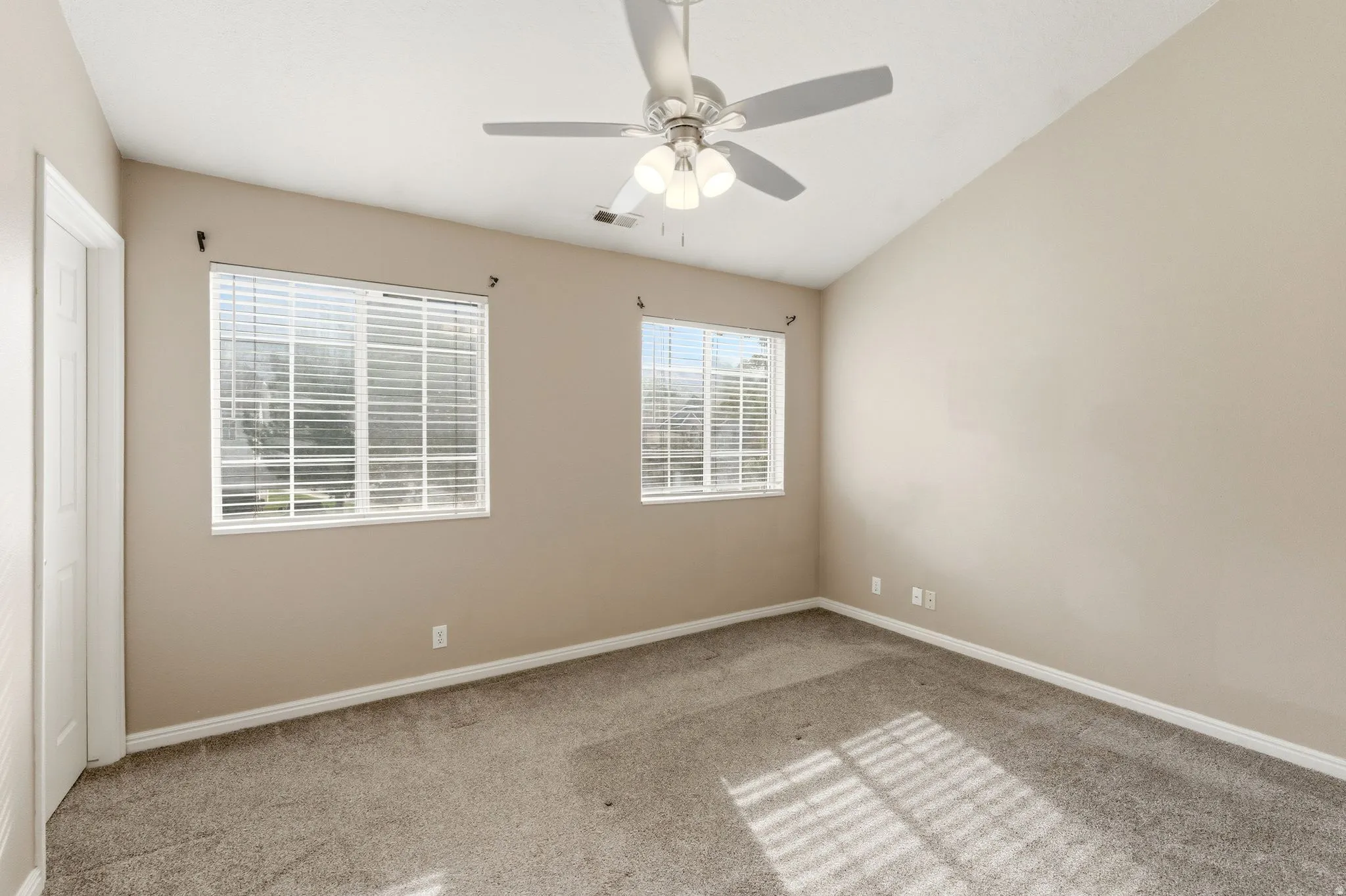 Spare room featuring ceiling fan, light carpet, and vaulted ceiling