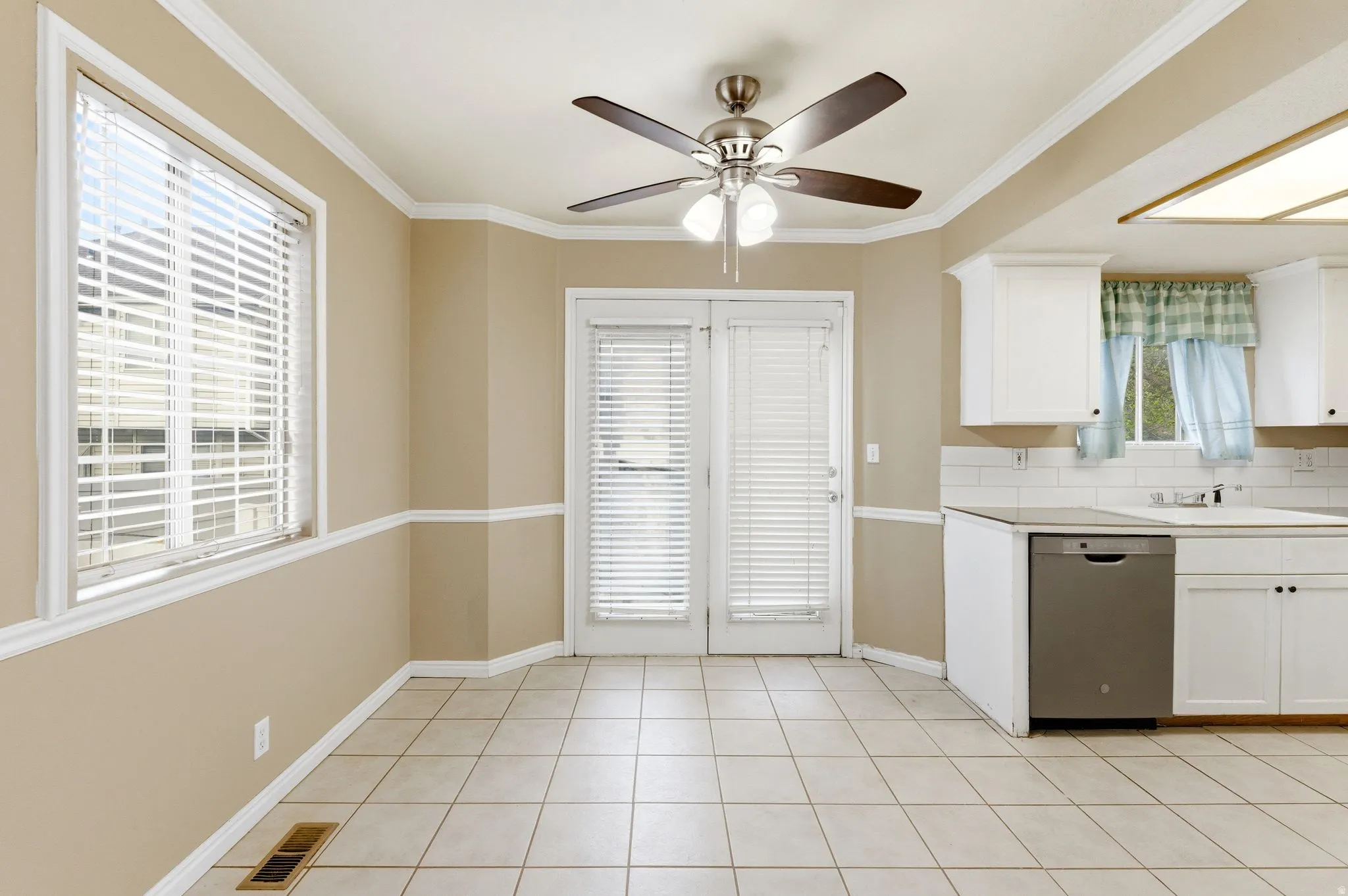 Kitchen with white cabinetry, stainless steel dishwasher, a ceiling fan, crown molding, and light countertops