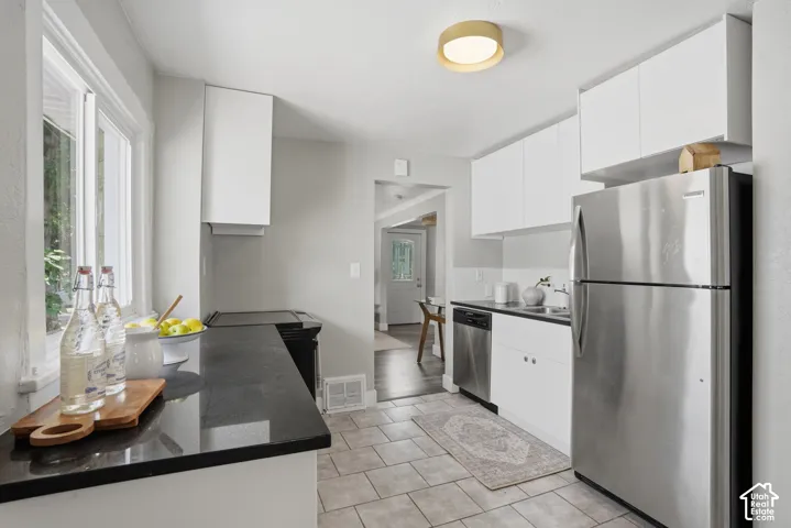 Kitchen featuring white cabinetry, stainless steel appliances, black countertops, and a tile floor
