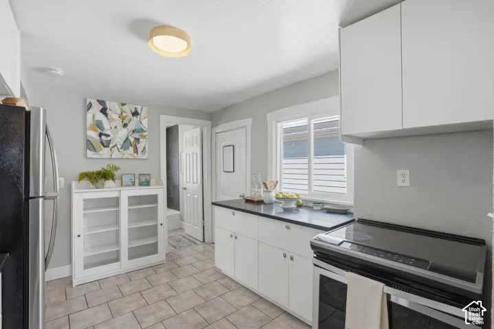 Contemporary kitchen featuring light gray walls, white cabinetry, dark countertops, a stainless steel refrigerator, and tiled flooring