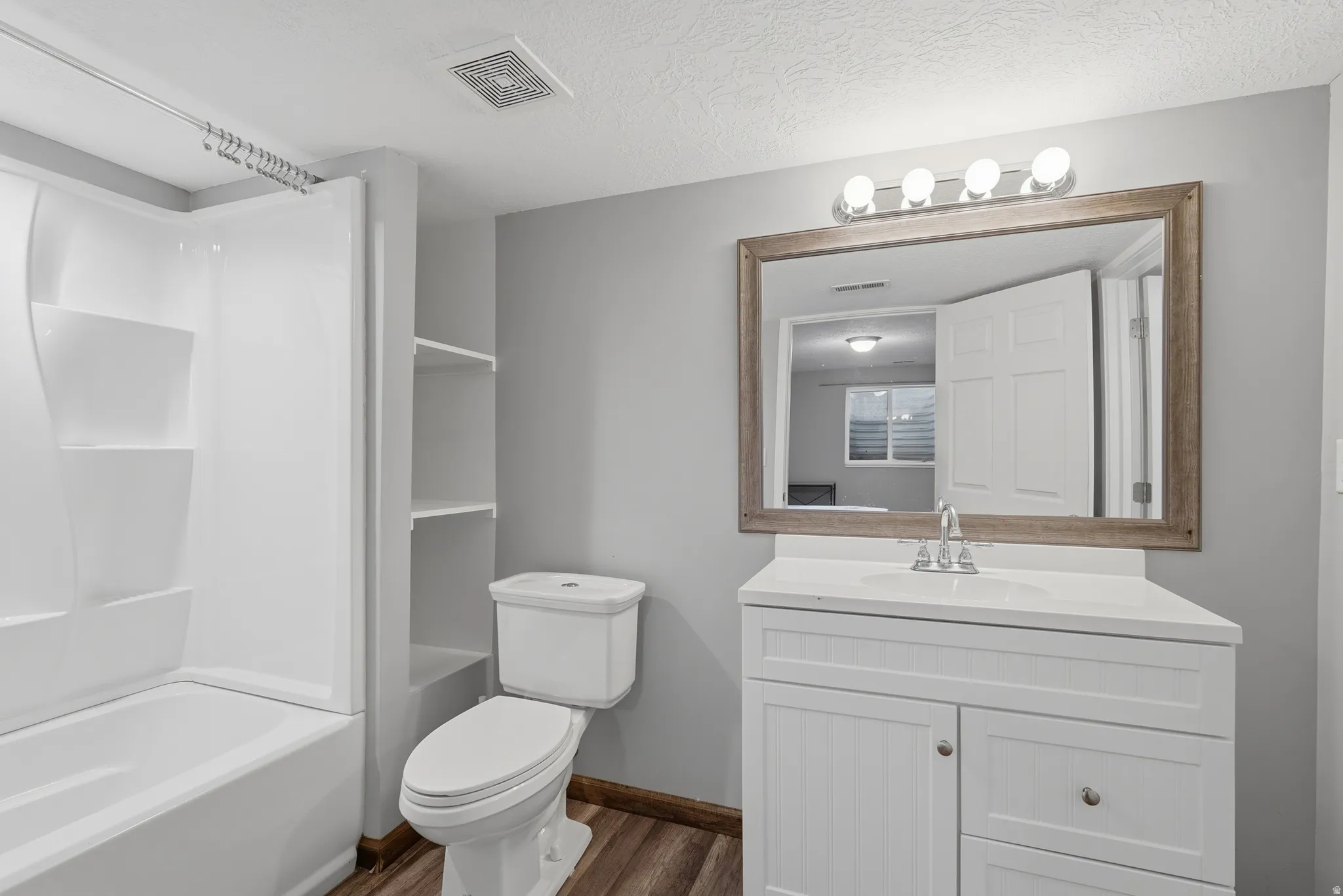 Bathroom with vanity, shower / bath combination, a textured ceiling, and dark wood-type flooring