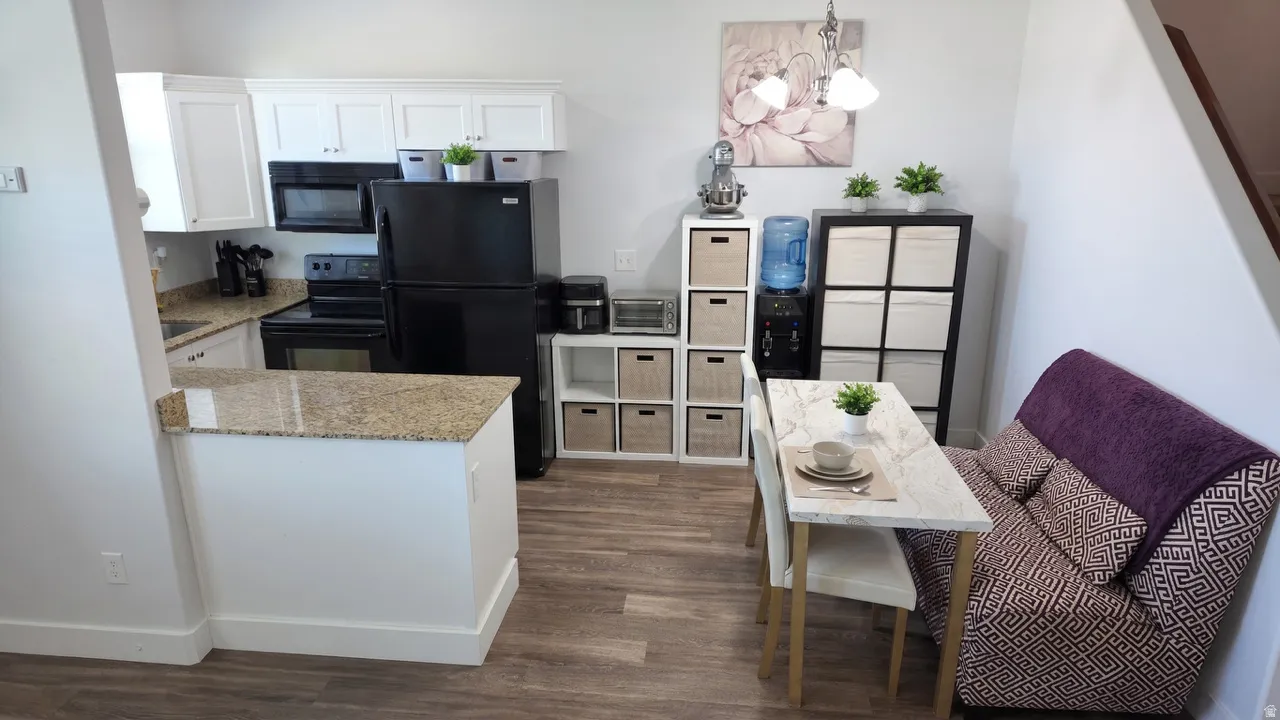 Kitchen with white cabinets, black appliances, suspended lighting, light stone countertops, and dark wood finished floors