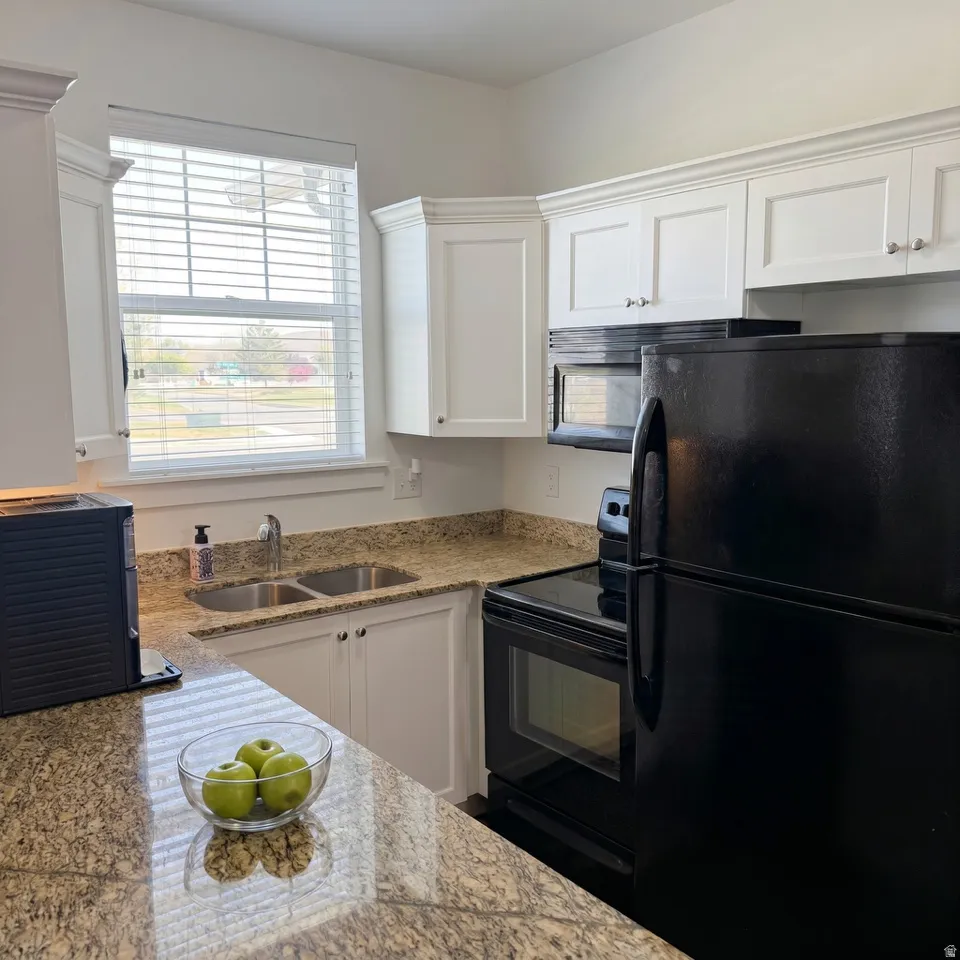 Kitchen with black appliances, white cabinetry, and light stone countertops