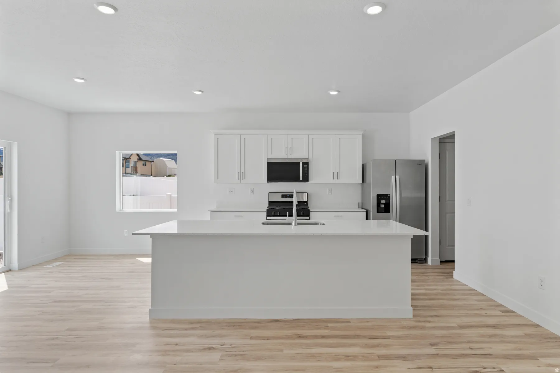 Bright kitchen featuring a central island with an integrated sink, white cabinetry with silver hardware, and stainless steel appliances