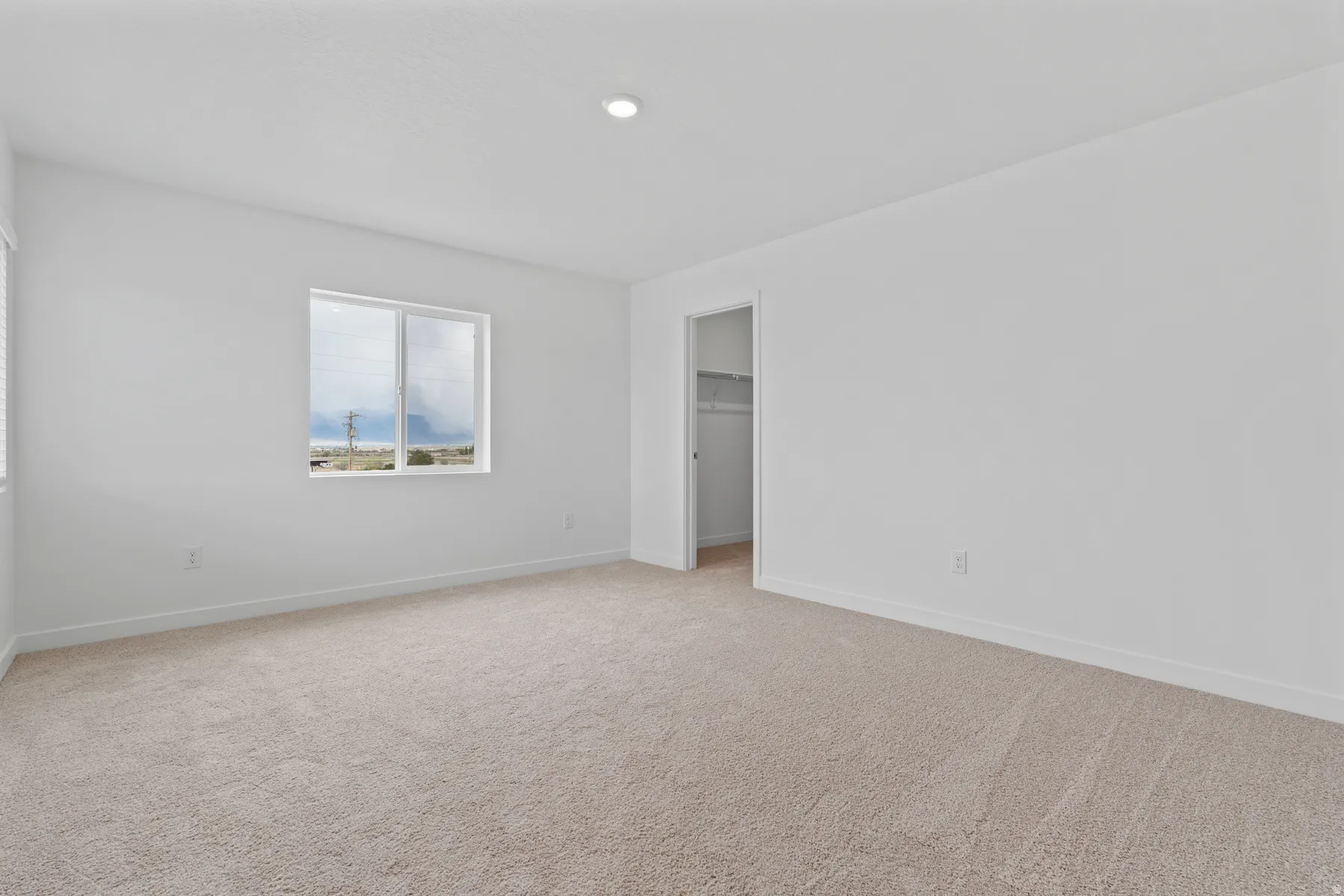 Carpeted interior space featuring a window with a white frame, recessed lighting, and a closet with shelving