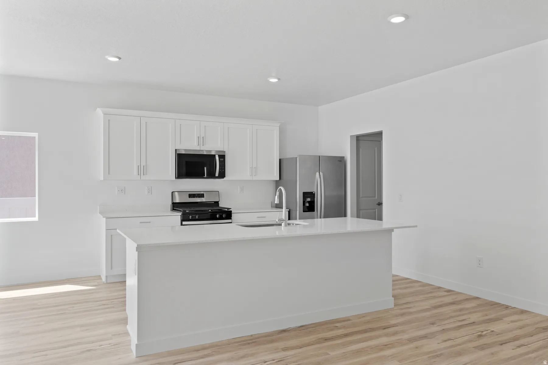 Kitchen featuring a central island with an integrated sink, white cabinetry, stainless steel appliances, wood-finish flooring, and recessed lighting