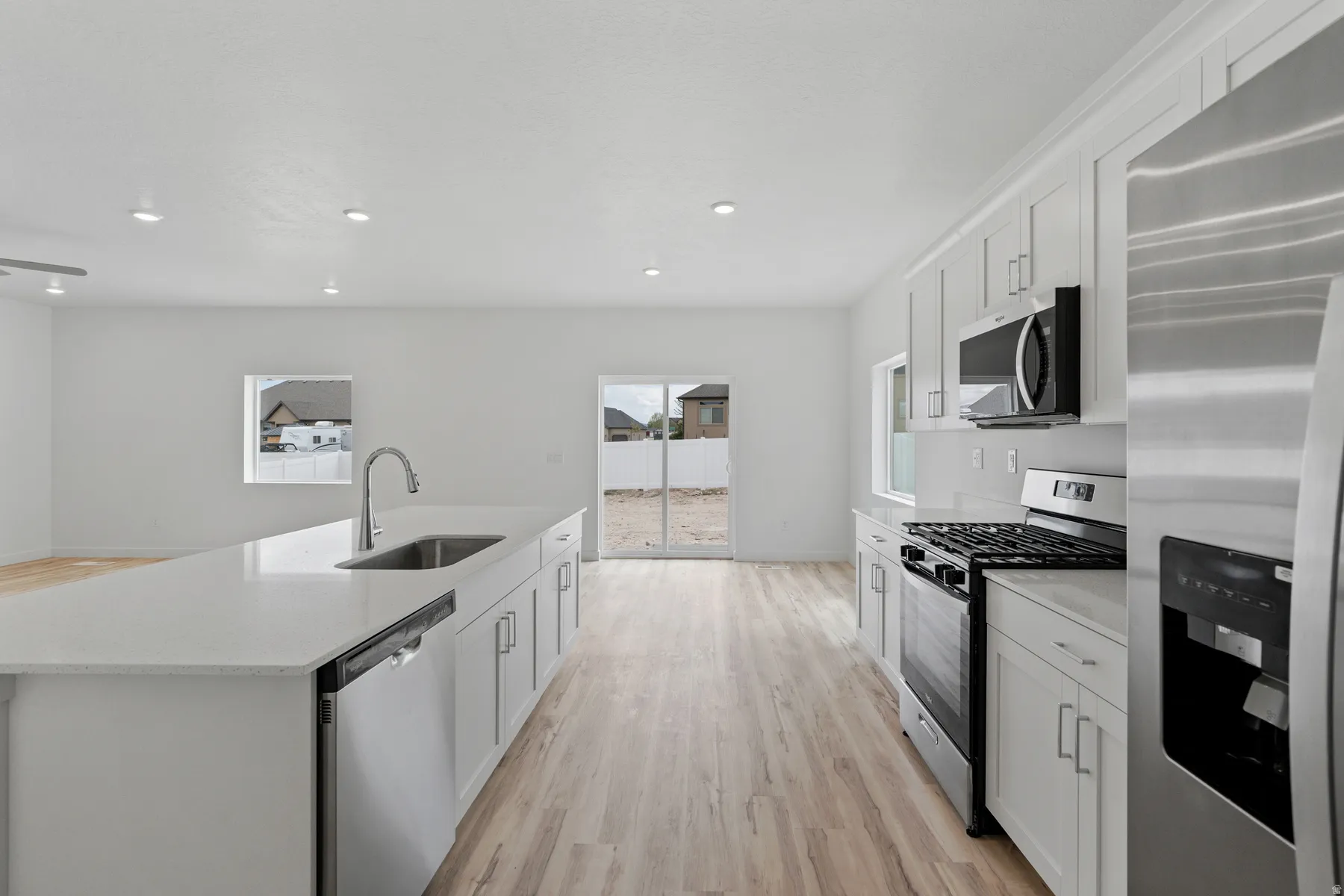 Bright kitchen featuring a substantial island with an integrated sink, stainless steel appliances, white cabinetry with crown molding, and wood-finish flooring