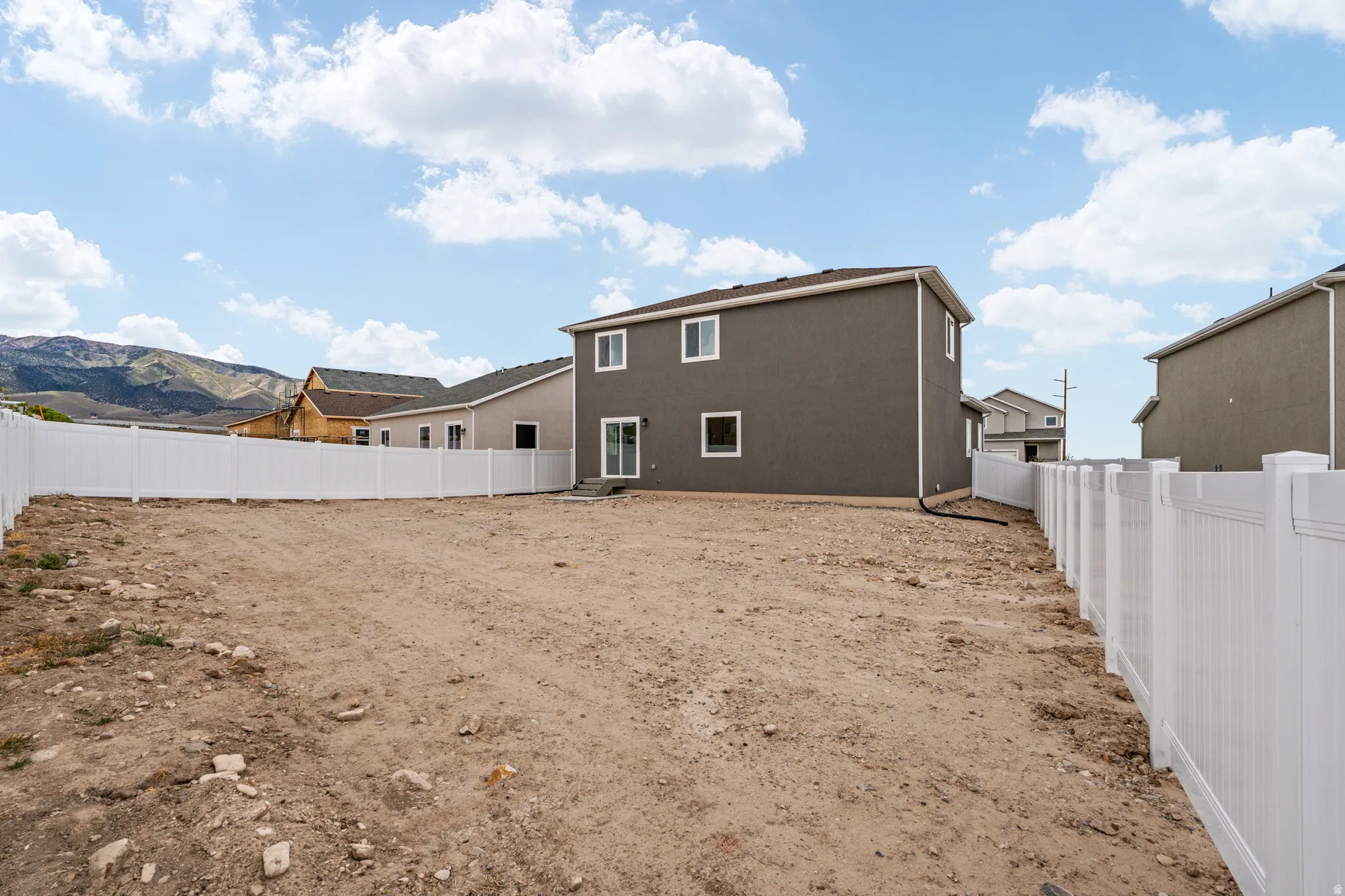 Expansive backyard lot featuring a white vinyl privacy fence and a mountain backdrop