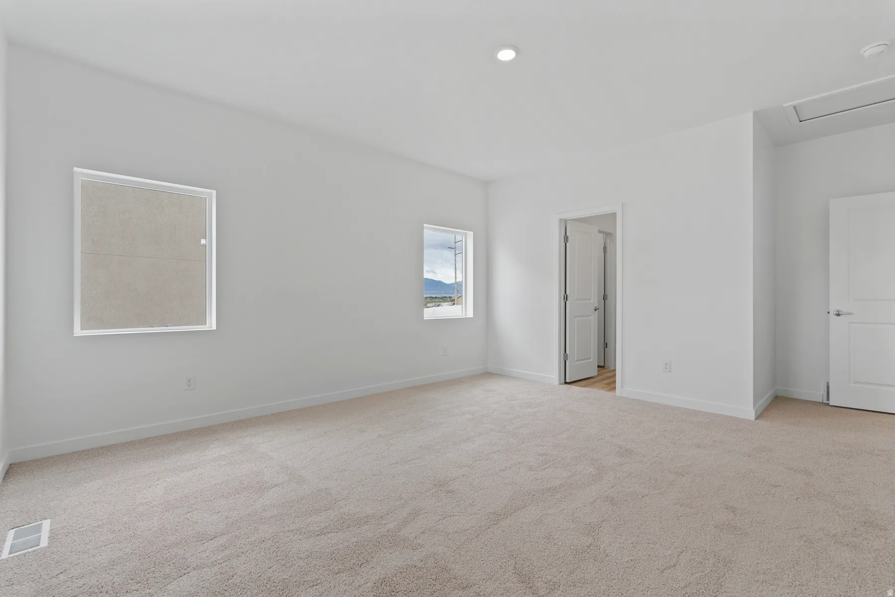 Spacious room featuring neutral carpeting, white painted walls, two windows, recessed lighting, and white baseboards