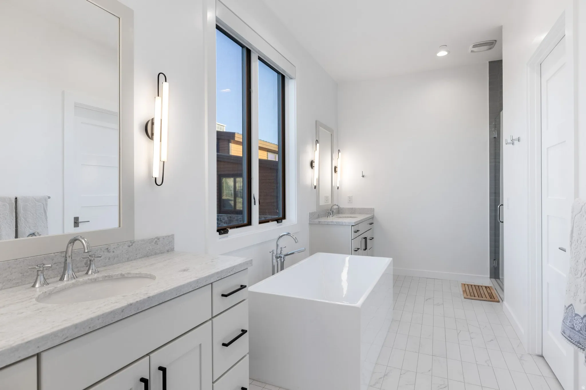 Bathroom featuring two vanities, a freestanding bath, a stall shower, and recessed lighting