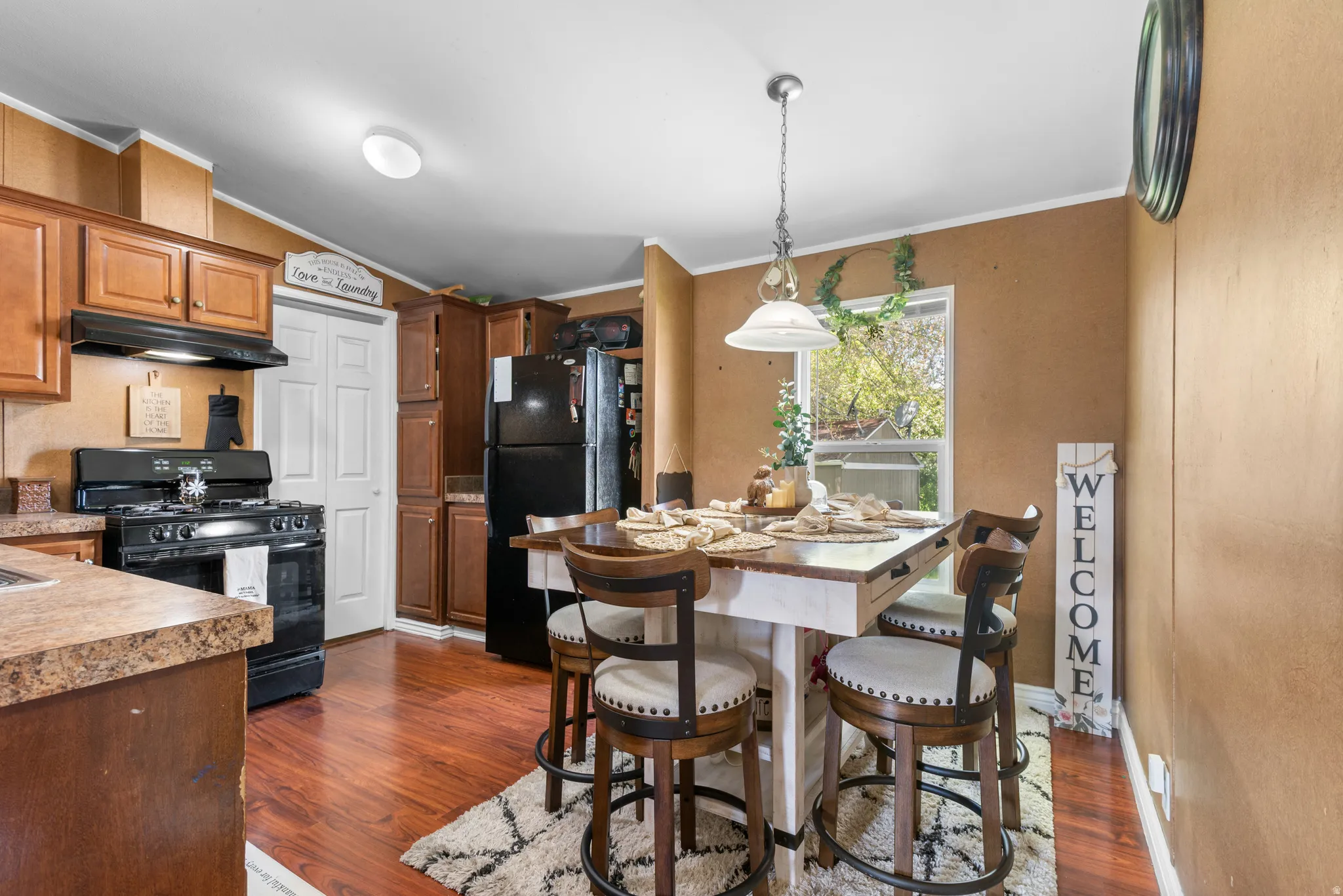 Kitchen with crown molding, black appliances, dark wood-type flooring, pendant lighting, and vaulted ceiling