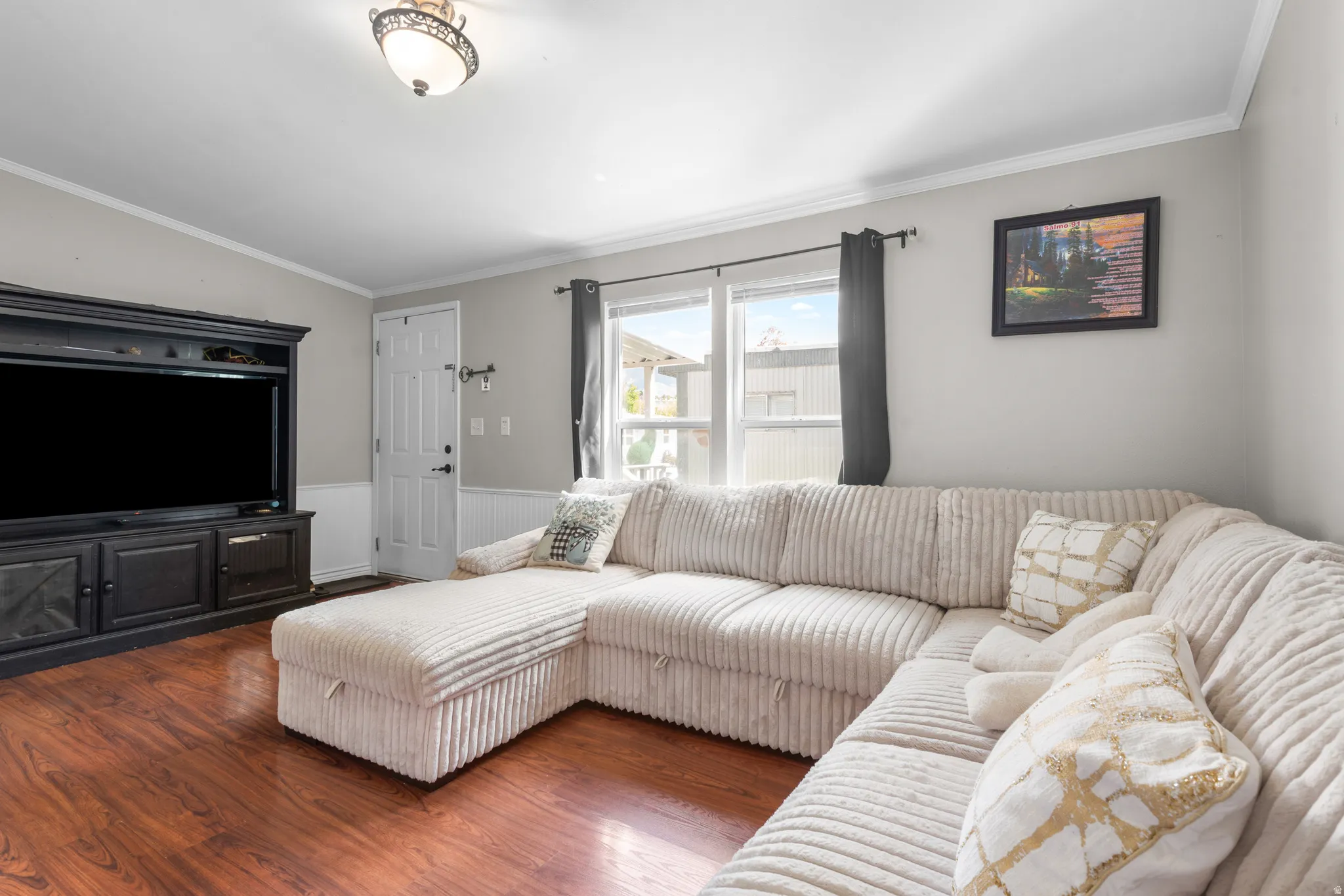 Living area featuring wainscoting, ornamental molding, wood finished floors, and lofted ceiling