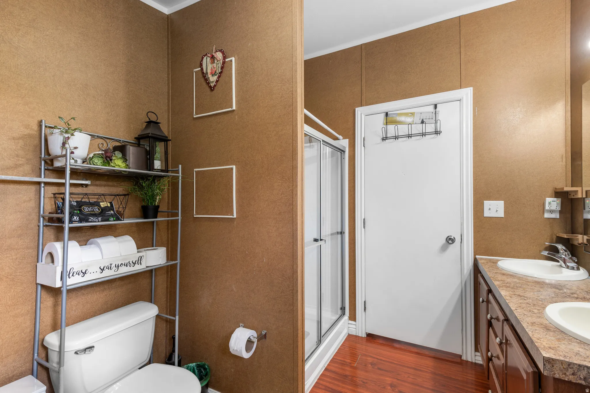 Full bathroom featuring a stall shower, double vanity, dark wood-style floors, and ornamental molding