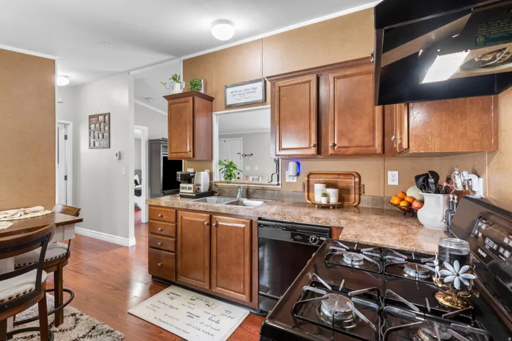 Kitchen featuring black appliances, range hood, light countertops, wood finish cabinets, and crown molding