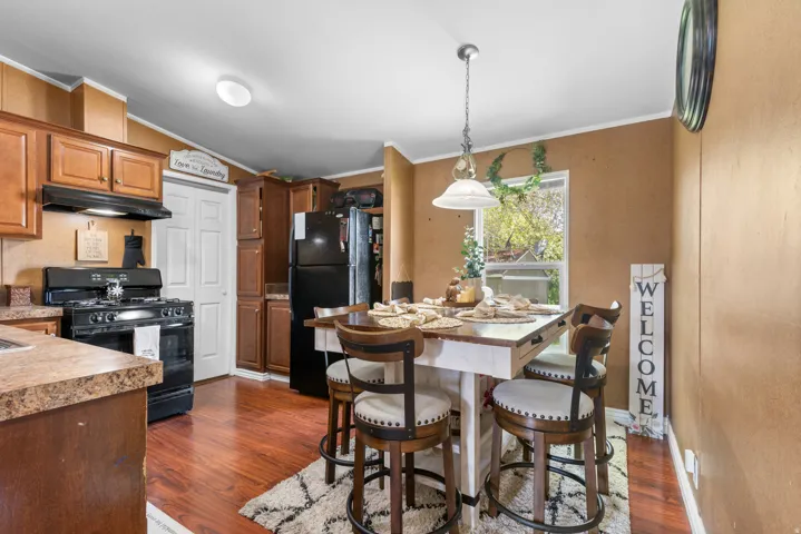 Kitchen with crown molding, black appliances, dark wood-type flooring, pendant lighting, and vaulted ceiling