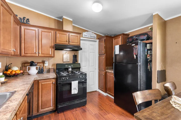 Kitchen featuring black appliances, ornamental molding, lofted ceiling, wood finish cabinets, and light countertops