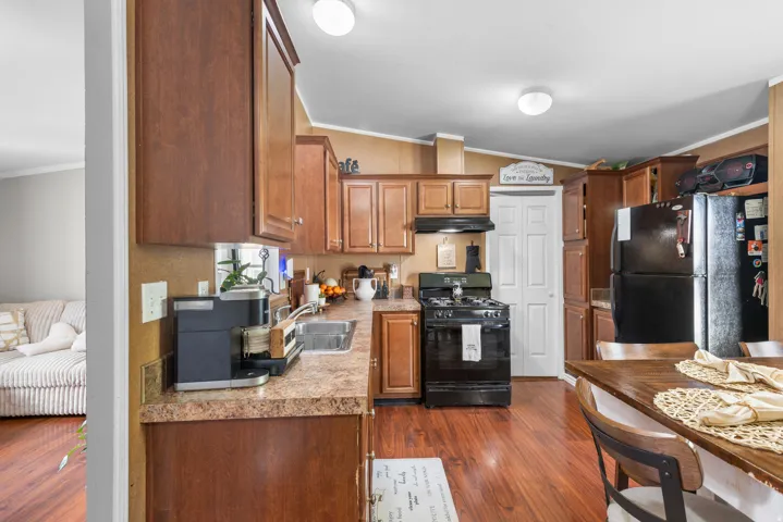 Kitchen featuring ornamental molding, black appliances, light countertops, dark wood-style floors, and wood finish cabinets