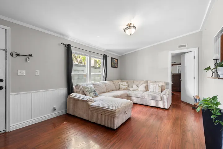 Living room featuring wood finished floors, crown molding, and a wainscoted wall