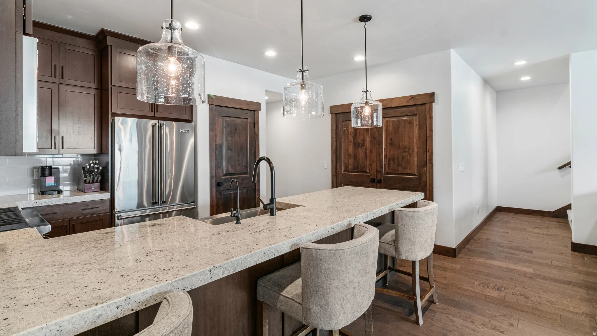 Kitchen with light stone countertops, stainless steel appliances, a peninsula, dark wood-type flooring, and a breakfast bar area