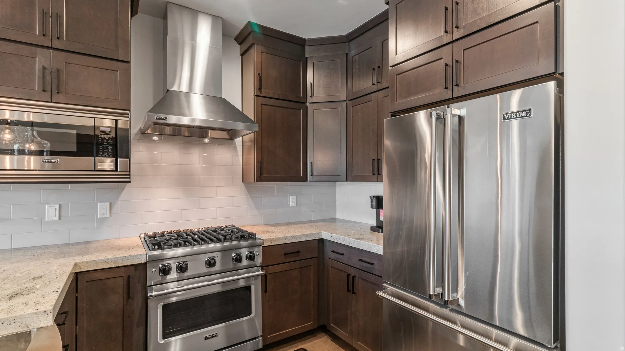 Kitchen with premium appliances, dark wood finish cabinets, backsplash, and light stone countertops