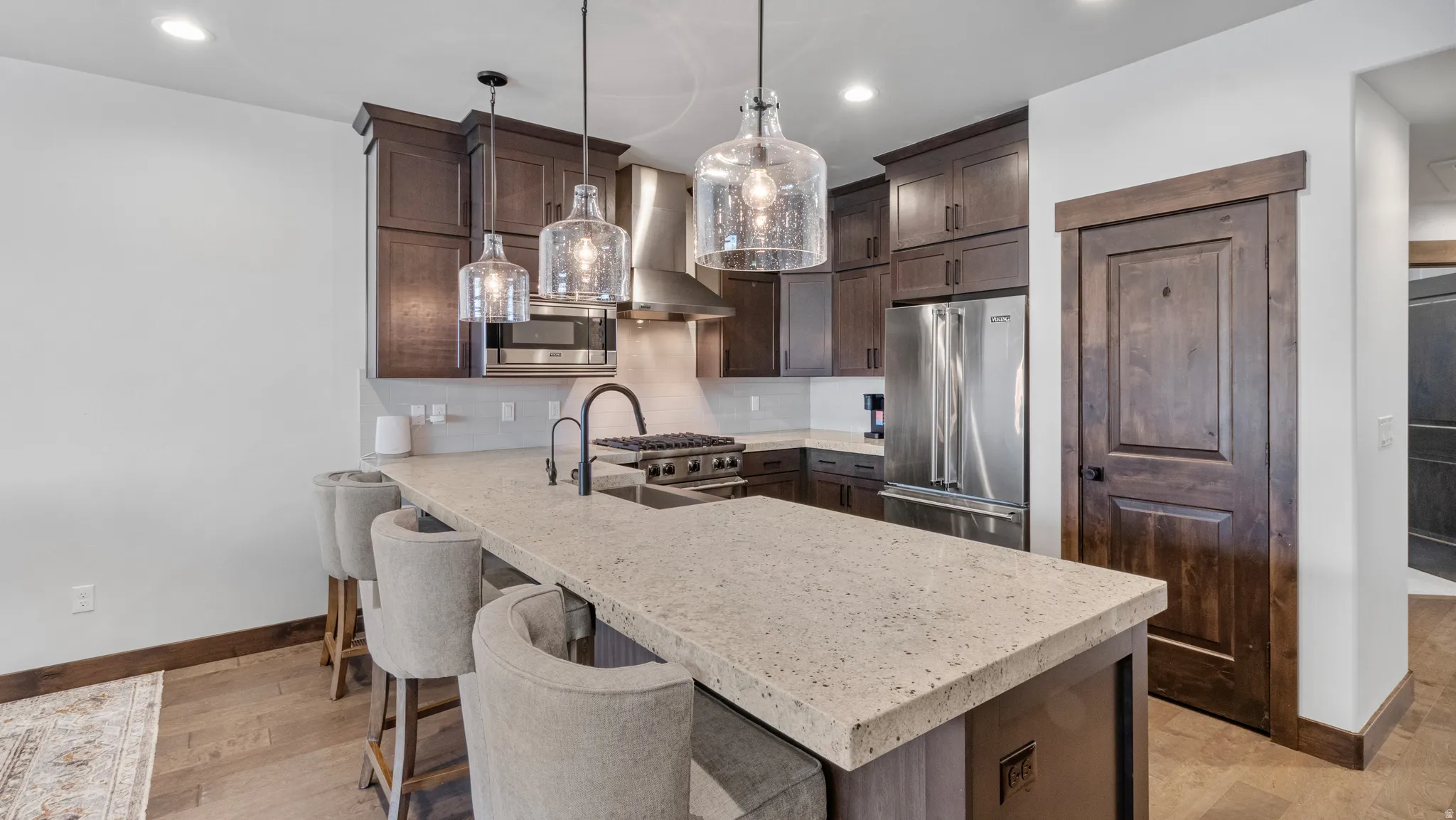 Kitchen with dark wood finish cabinets, a kitchen bar, stainless steel appliances, a peninsula, and light stone countertops
