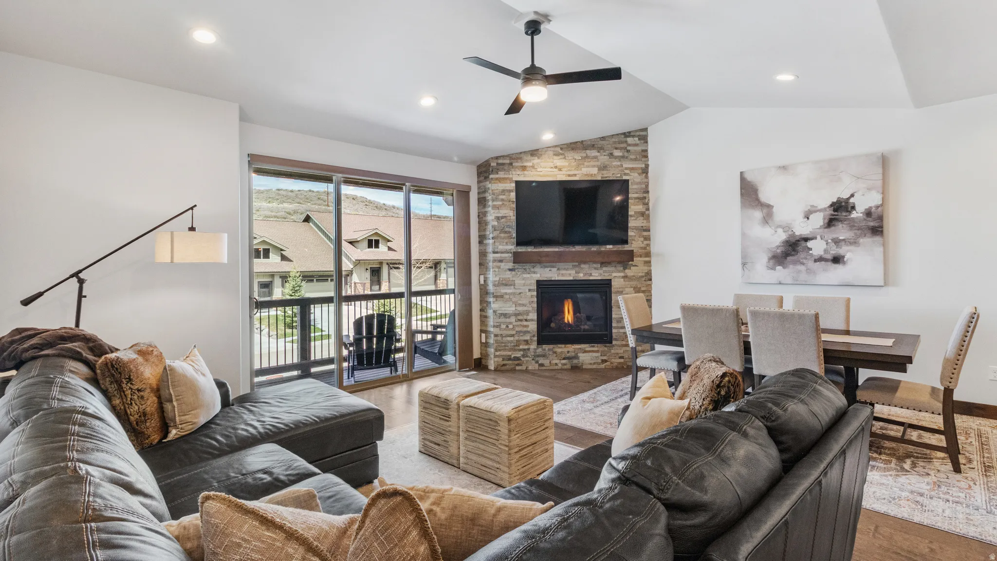 Living area with wood finished floors, a ceiling fan, a stone fireplace, vaulted ceiling, and recessed lighting