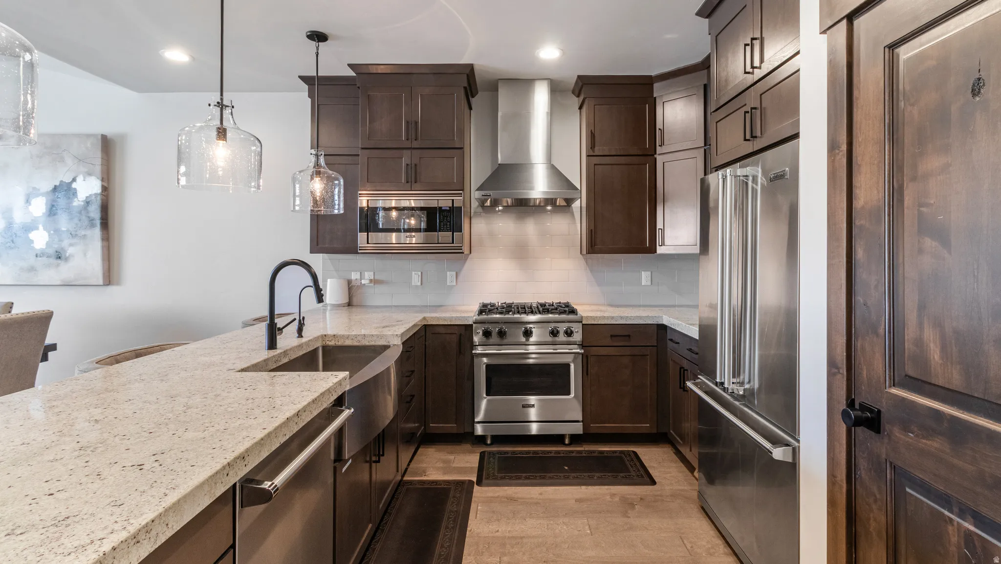 Kitchen featuring premium appliances, pendant lighting, dark wood finish cabinetry, light stone countertops, and light wood-style floors